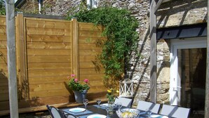 An outdoor dining area with a wooden table set for four, surrounded by stone walls and a wooden fence.