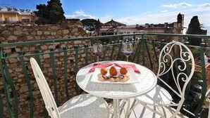Un balcon avec une table dressée pour deux personnes, sur laquelle on trouve une assiette de croquettes et deux verres de vin rouge.