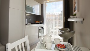 Une cuisine compacte avec des meubles blancs, une table à manger avec des chaises et un petit balcon avec vue.