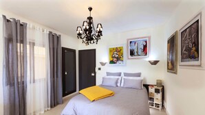 Une chambre à coucher avec un lit, des rideaux, un lustre et des œuvres d’art accrochées aux murs.