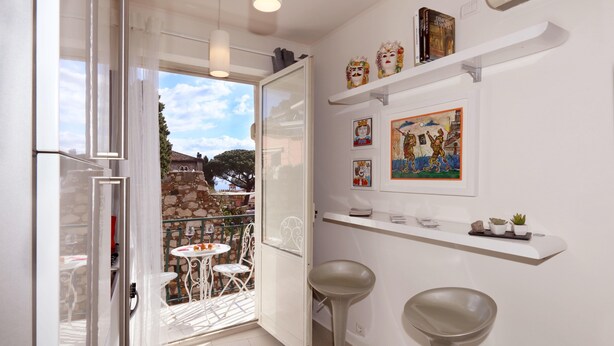 Une cuisine moderne avec des meubles blancs, un coin repas comprenant une table et des chaises, et un balcon offrant une vue sur les environs.
