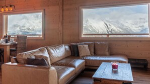 Een gezellige woonkamer met een leren bank, een houten salontafel en grote ramen met uitzicht op besneeuwde bergen.