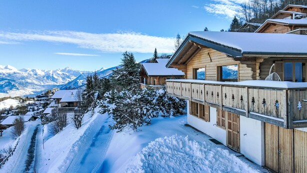 Een houten chalet met een balkon met uitzicht op een besneeuwd berglandschap.