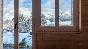 Een houten chalet met grote ramen, met uitzicht op besneeuwde bergen en bomen.