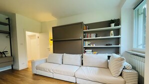 A modern living room with a sofa, a bookshelf, and a window. - Green view … green in the city  (Bolzano)