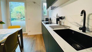 A modern kitchen with a black sink, white marble countertop, and a window overlooking greenery. - Green view … green in the city  (Bolzano)