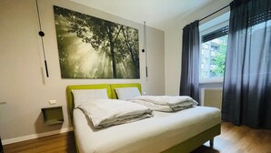 A bedroom with a bed, a wall-mounted light, a power outlet, and a window with curtains. - Green view … green in the city  (Bolzano)
