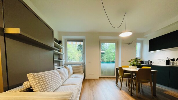 A modern living space with a sofa, dining table, chairs, and a kitchen area. - Green view … green in the city  (Bolzano)