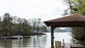 En paviljong vid sjön med en bänk och ett picknickbord, omgiven av träd och båtar som ligger förtöjda.