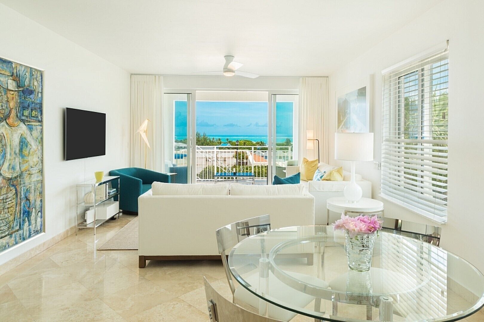 Uma sala de estar moderna com uma mesa de vidro, sofás brancos e vista para o mar.