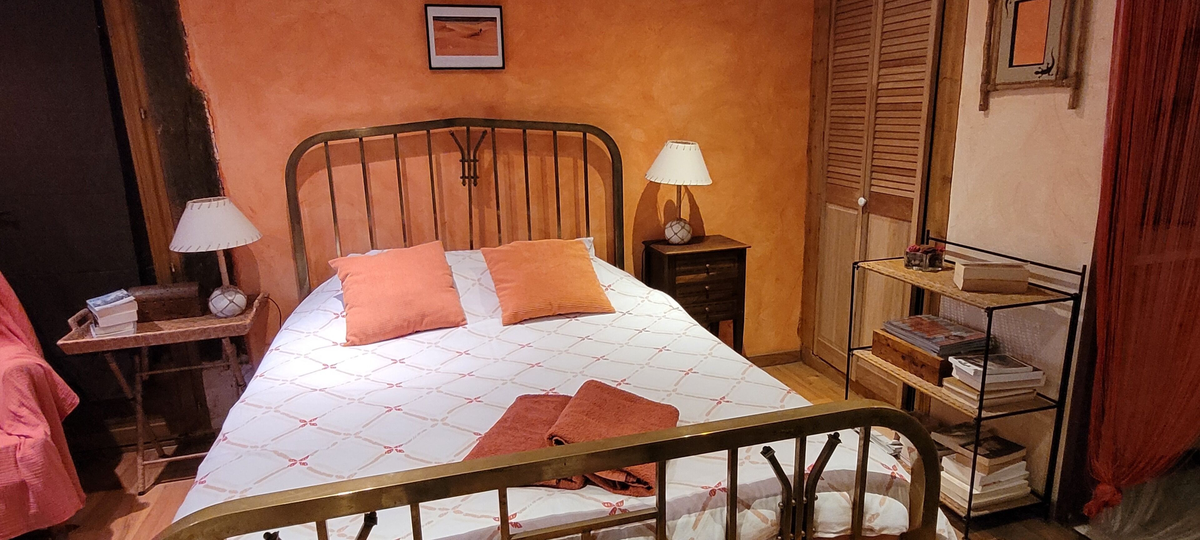 Ein Schlafzimmer mit einem Bett, zwei Nachttischen, einem Regal mit Büchern und einem Fenster mit Fensterläden.