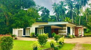 A two-story house with a front porch, surrounded by lush greenery and palm trees. - The  Nature  Holiday  Home (Baddegama)