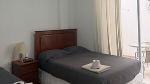 A hotel room with a bed, a bedside table with a lamp, a remote control, and a roll of toilet paper on the bed. - Blanca Rosa's Place Vacation Rentals (Pacasmayo)