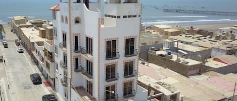 A multi-story building with balconies, a parking area, and a view of the beach and sea.