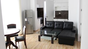 A modern living room with a glass coffee table, a black leather sofa, and a dining area with a round table and chairs. - Blanca Rosa's Place Vacation Rentals (Pacasmayo)