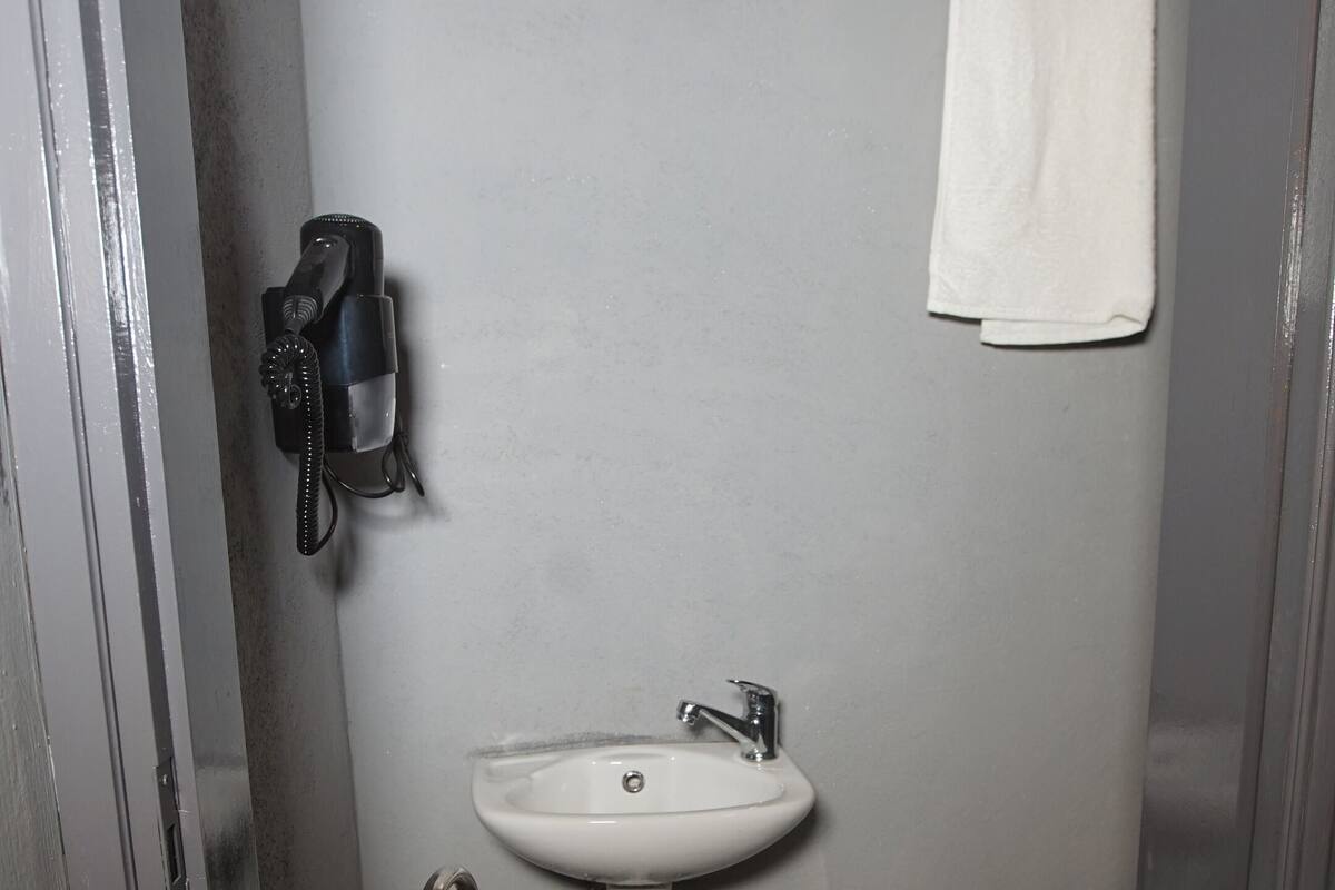 A small bathroom with a white sink, a toilet, and a blue trash can.