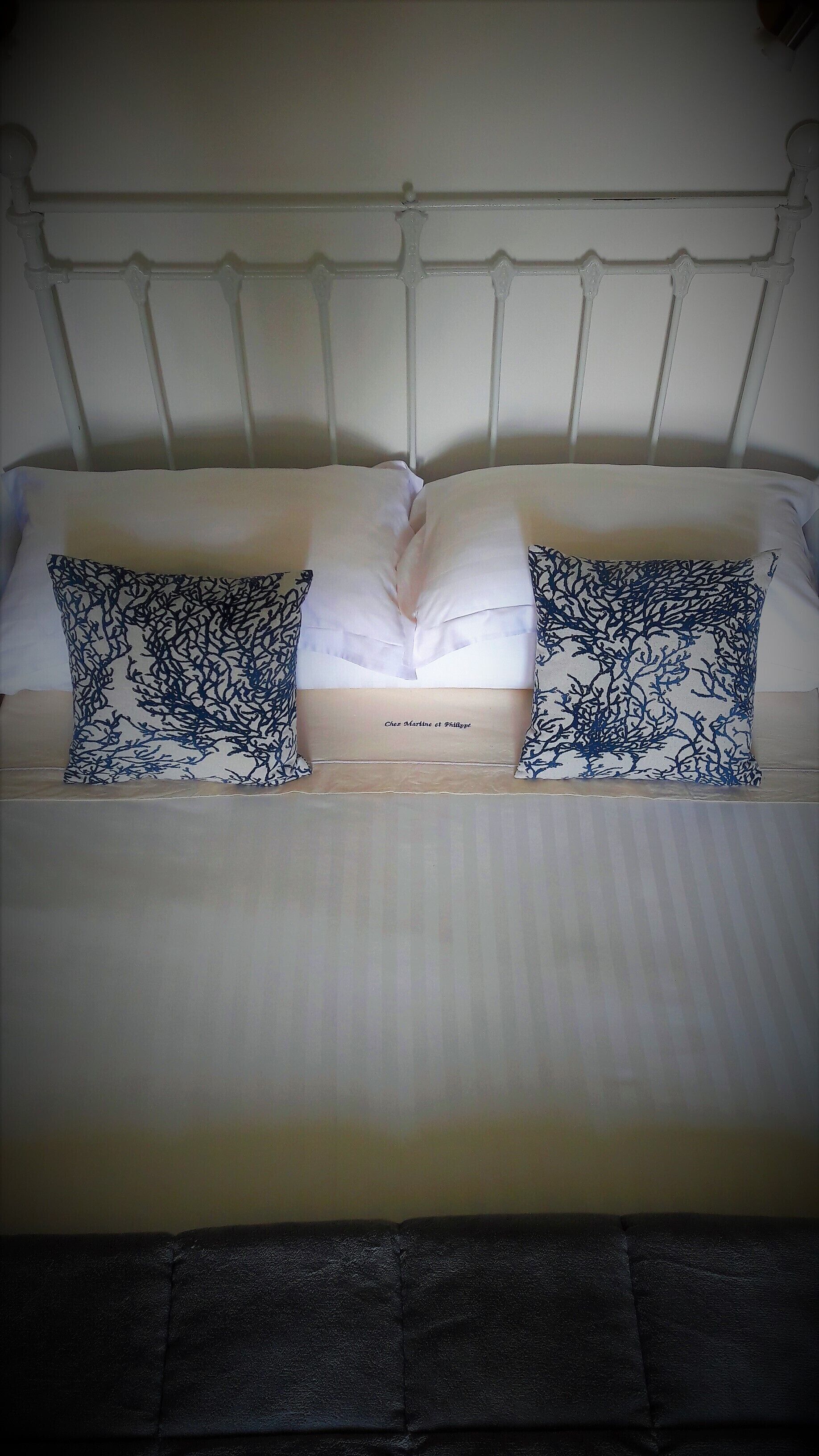 Una cama con ropa blanca, dos almohadas decorativas con un estampado azul y un cabecero de diseño sencillo.