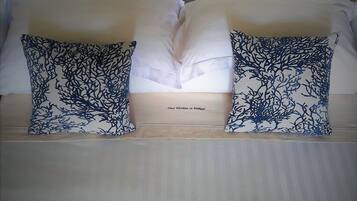 Una cama con ropa blanca, dos almohadas decorativas con un estampado azul y un cabecero de diseño sencillo.