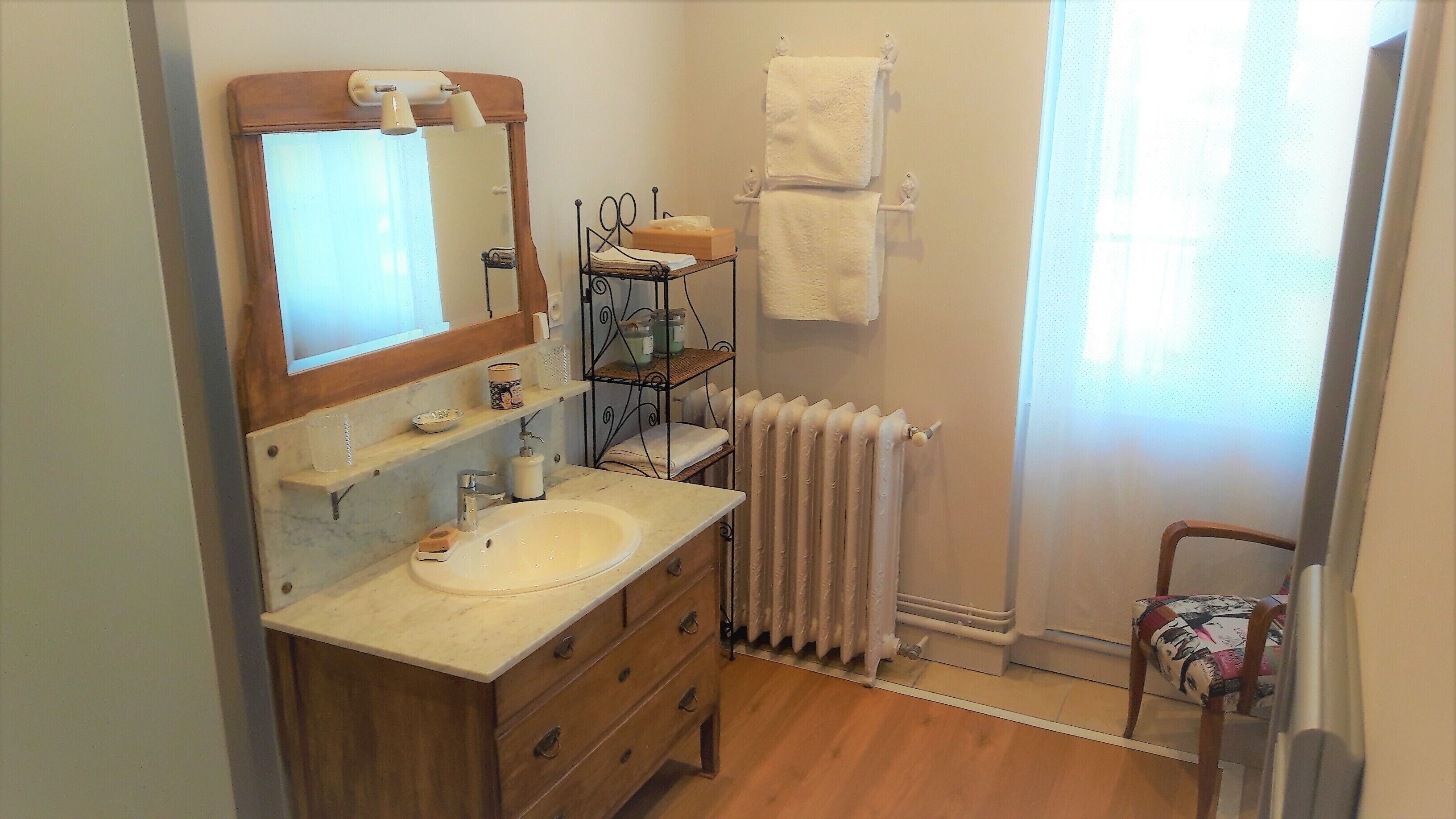 A bathroom with a wooden vanity, a sink, a mirror, a towel rack, a radiator, and a chair.