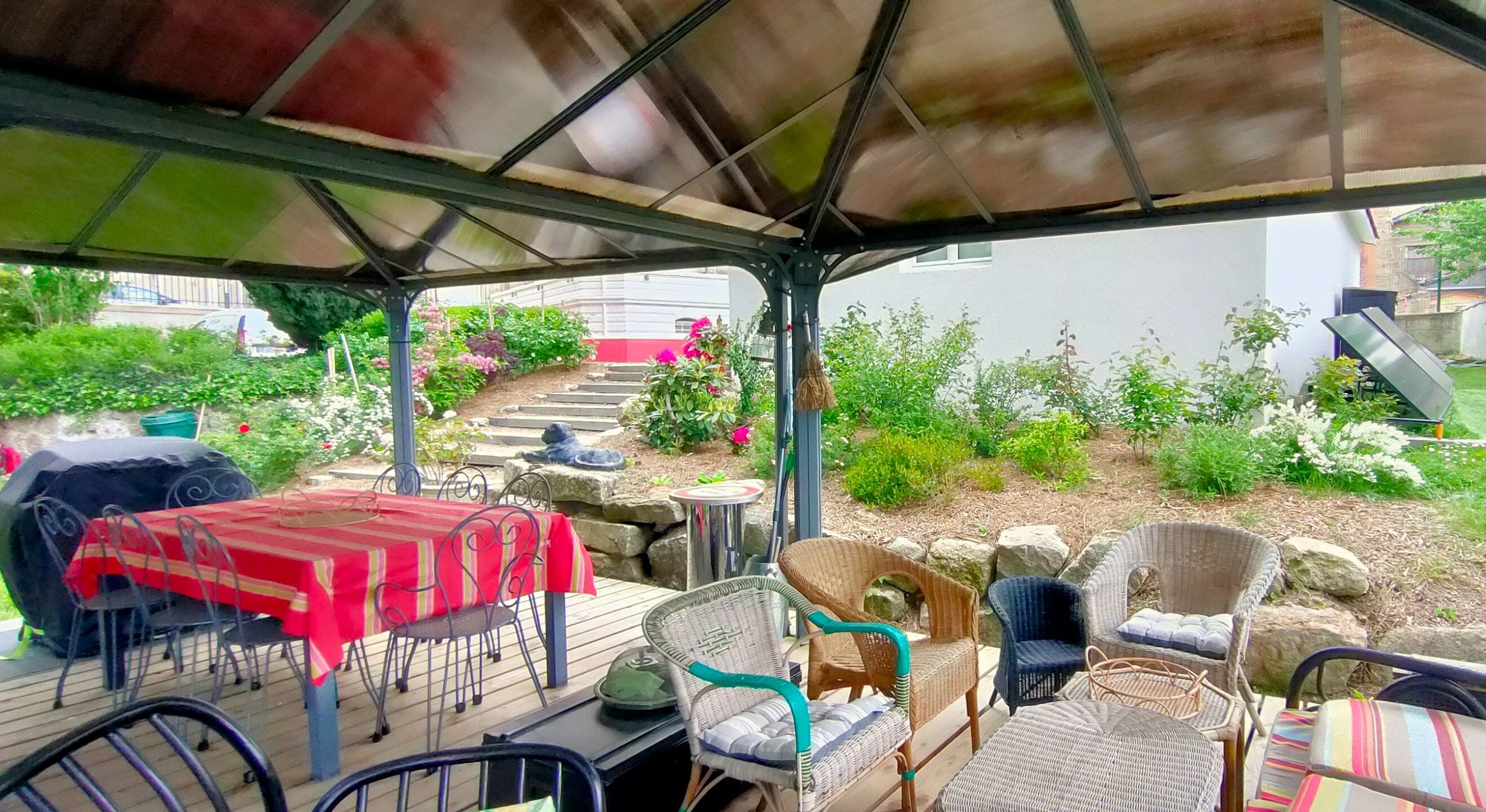 Une terrasse extérieure dotée d’un espace salon abrité, d’un barbecue et d’une variété de plantes et d’arbustes.