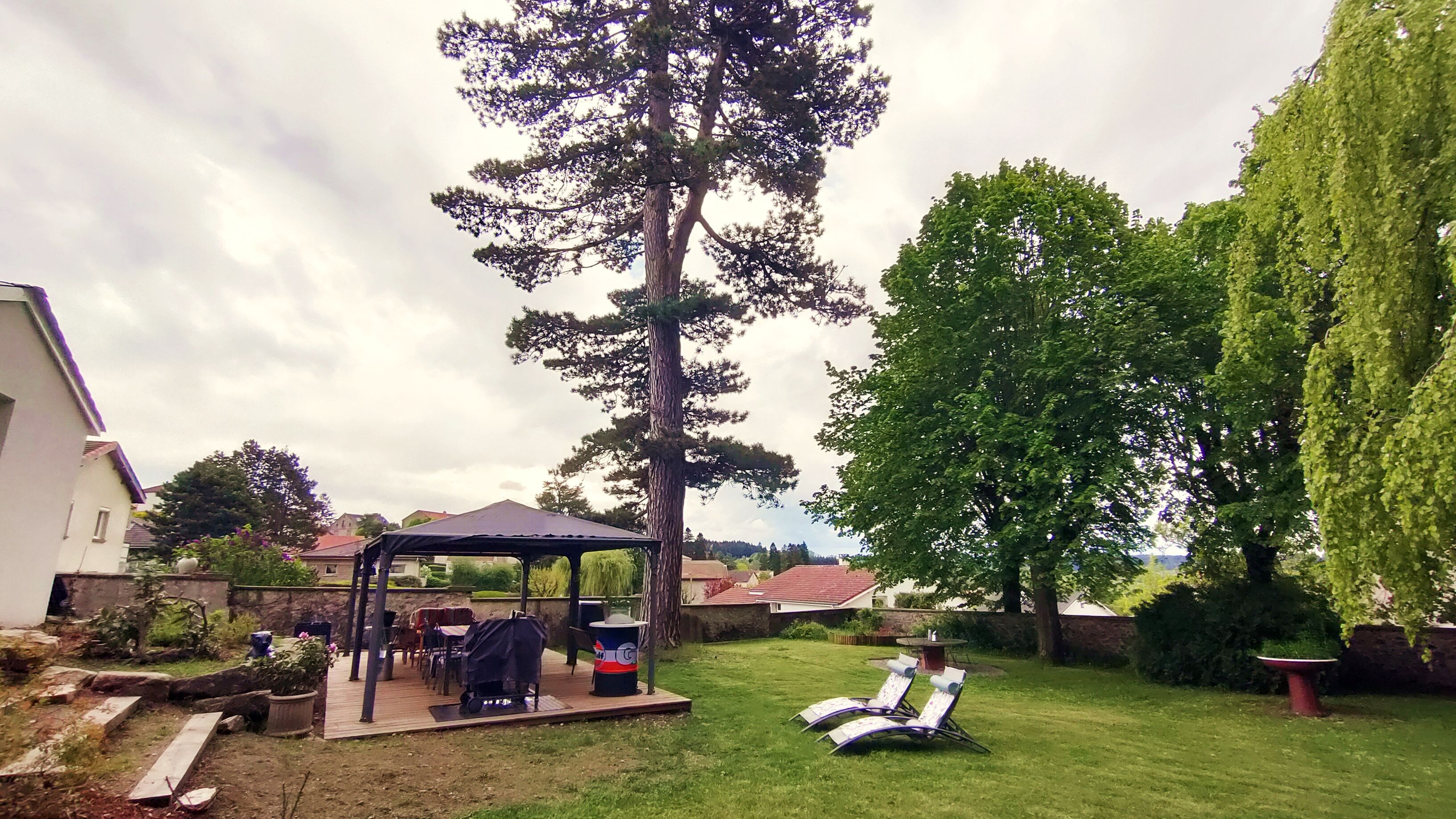 Un jardin avec un espace barbecue, une pergola et un coin salon équipé de deux fauteuils.