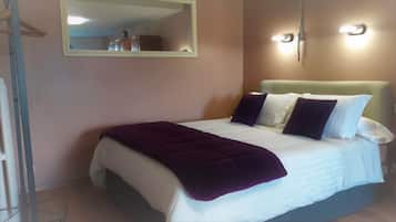 Un lit bien fait, avec une couverture violette, des oreillers blancs et une tête de lit. Un miroir est accroché au-dessus du lit et un luminaire est fixé au mur.