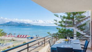Un balcone con tavolo apparecchiato per mangiare, affacciato su una spiaggia con una montagna sullo sfondo.