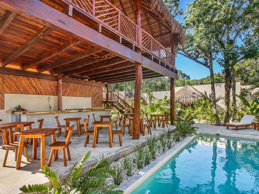 Un área junto a la piscina con mesas y sillas de madera, un bar y una piscina.