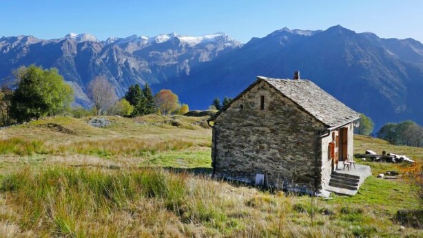 A stone cottage with a red door, set against a backdrop of mountains and clear blue sky. - Rustico Andrea by Interhome (Castro)