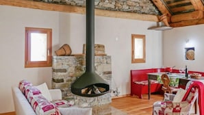 A cozy living room with a stone fireplace, wooden beams, and a dining area with red chairs. - Rustico Andrea by Interhome (Castro)