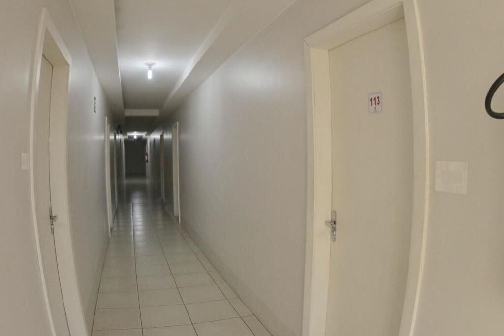 A narrow, well-lit hallway with white walls and tiled flooring, leading to multiple doors, each marked with a number.