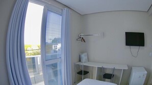 A hotel room with a bed, a desk, a chair, a TV, and a balcony with curtains. - Grande Hotel (Gurupi)