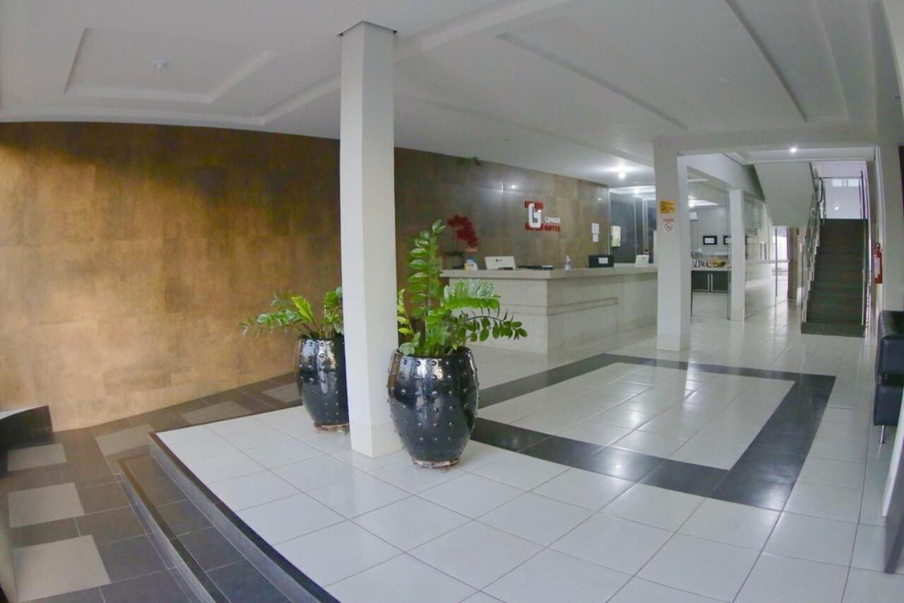 A hotel lobby with a reception desk, potted plants, and a tiled floor.
