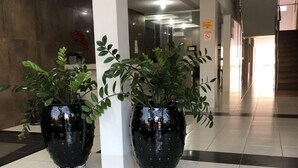 A modern lobby with two large black planters with green plants, white pillars, and a tiled floor. - Grande Hotel (Gurupi)