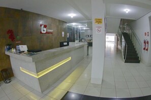 A hotel reception area with a modern design, including a reception desk, a staircase, and a sign indicating a smoking area. - Grande Hotel (Gurupi)