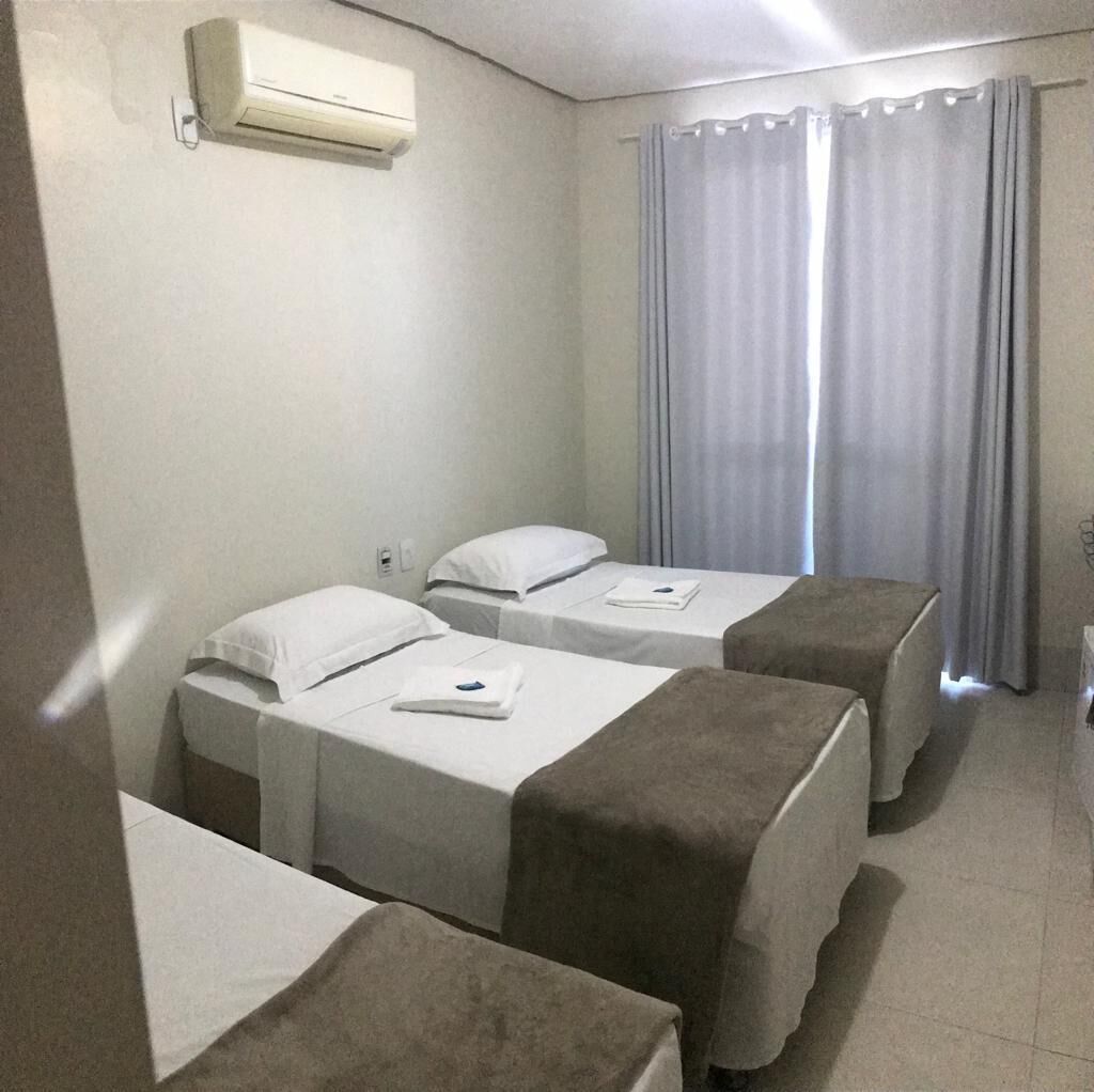 A hotel room with two single beds, a window with curtains, an air conditioning unit, and a tiled floor.