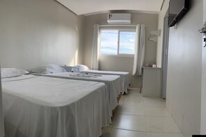 A hotel room with two single beds, a window with curtains, an air conditioning unit, and a TV mounted on the wall. - Grande Hotel (Gurupi)