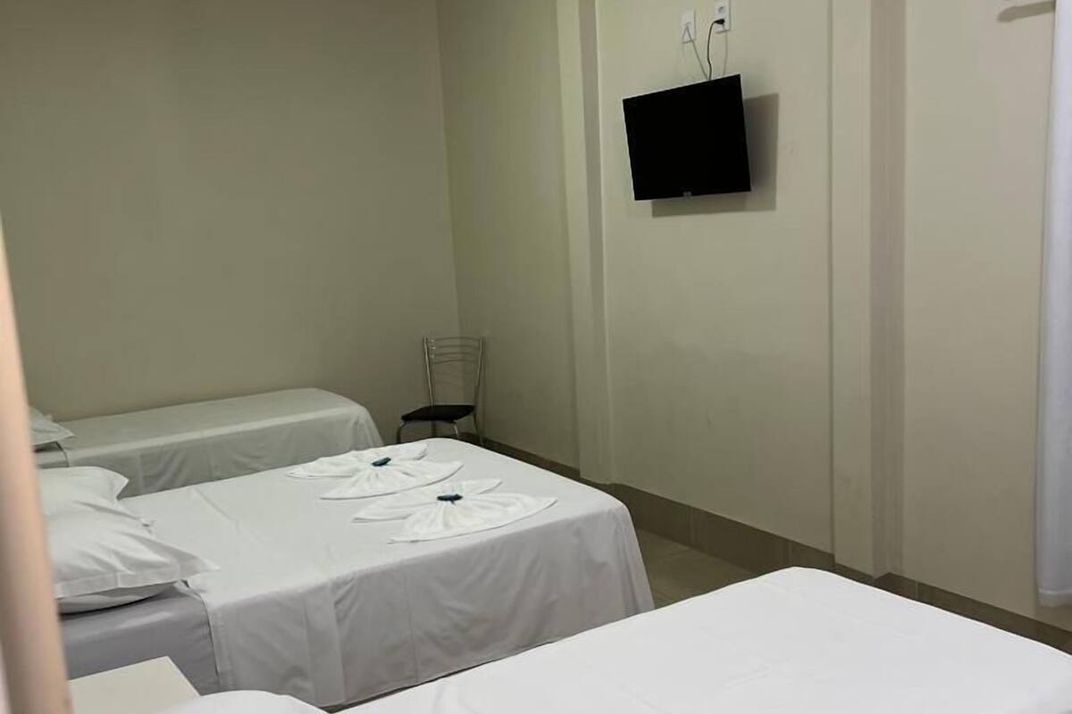 Una habitación de hotel con dos camas individuales, un televisor de pantalla plana montado en la pared y una mesita con una silla.