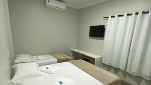 A hotel room with a bed, a bedside table, a TV, and a window with curtains. - Grande Hotel (Gurupi)