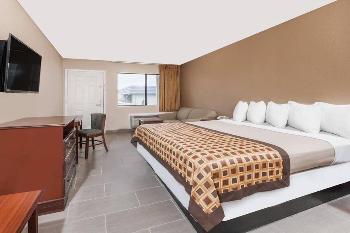 A hotel room with a bed, a desk, a chair, a TV, and a window with curtains.