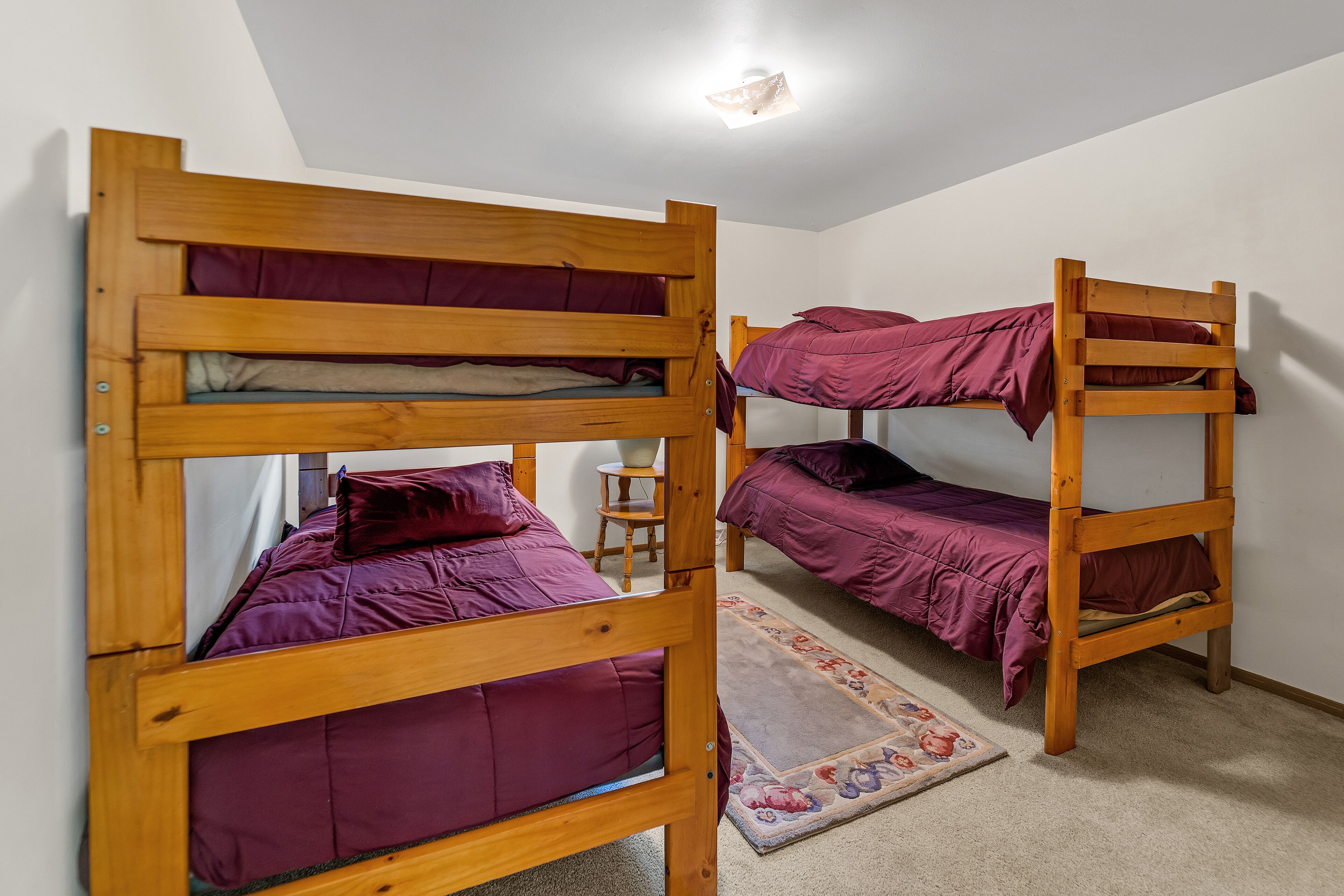 A room with two bunk beds, a small wooden stool, and a floral rug.
