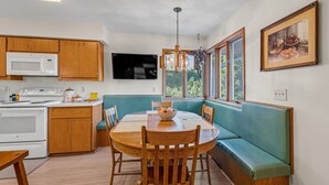 A kitchen with wooden cabinets, a microwave, a stove, a dining table with chairs, and a teal bench.