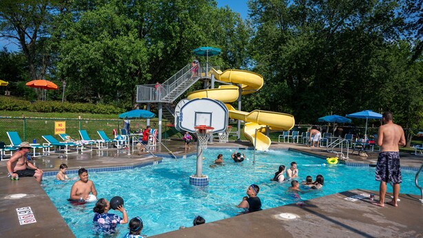 A swimming pool with a water slide, sun loungers, and a basketball hoop.