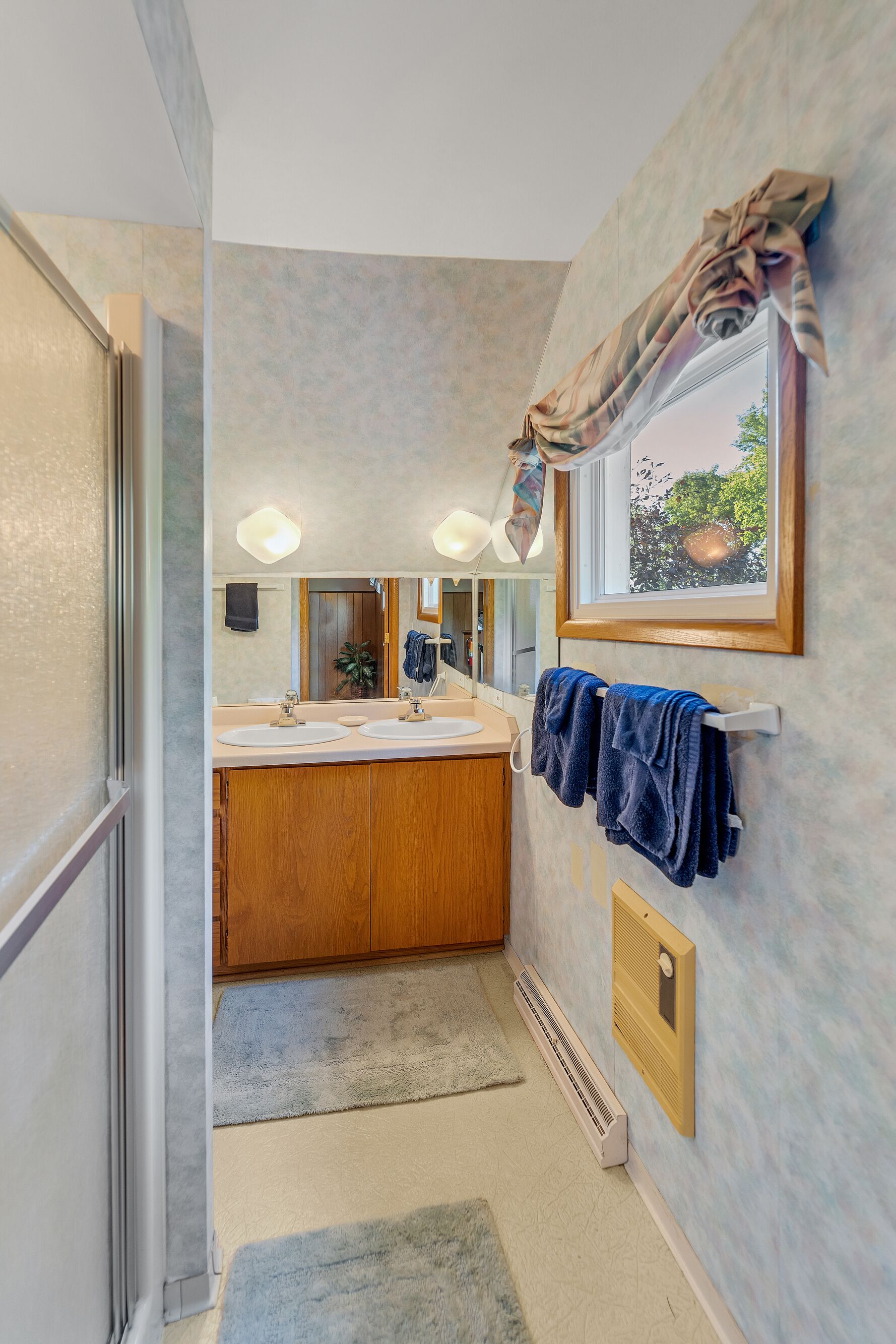 Une salle de bain avec un grand miroir, deux lavabos, un porte-serviettes et un radiateur.