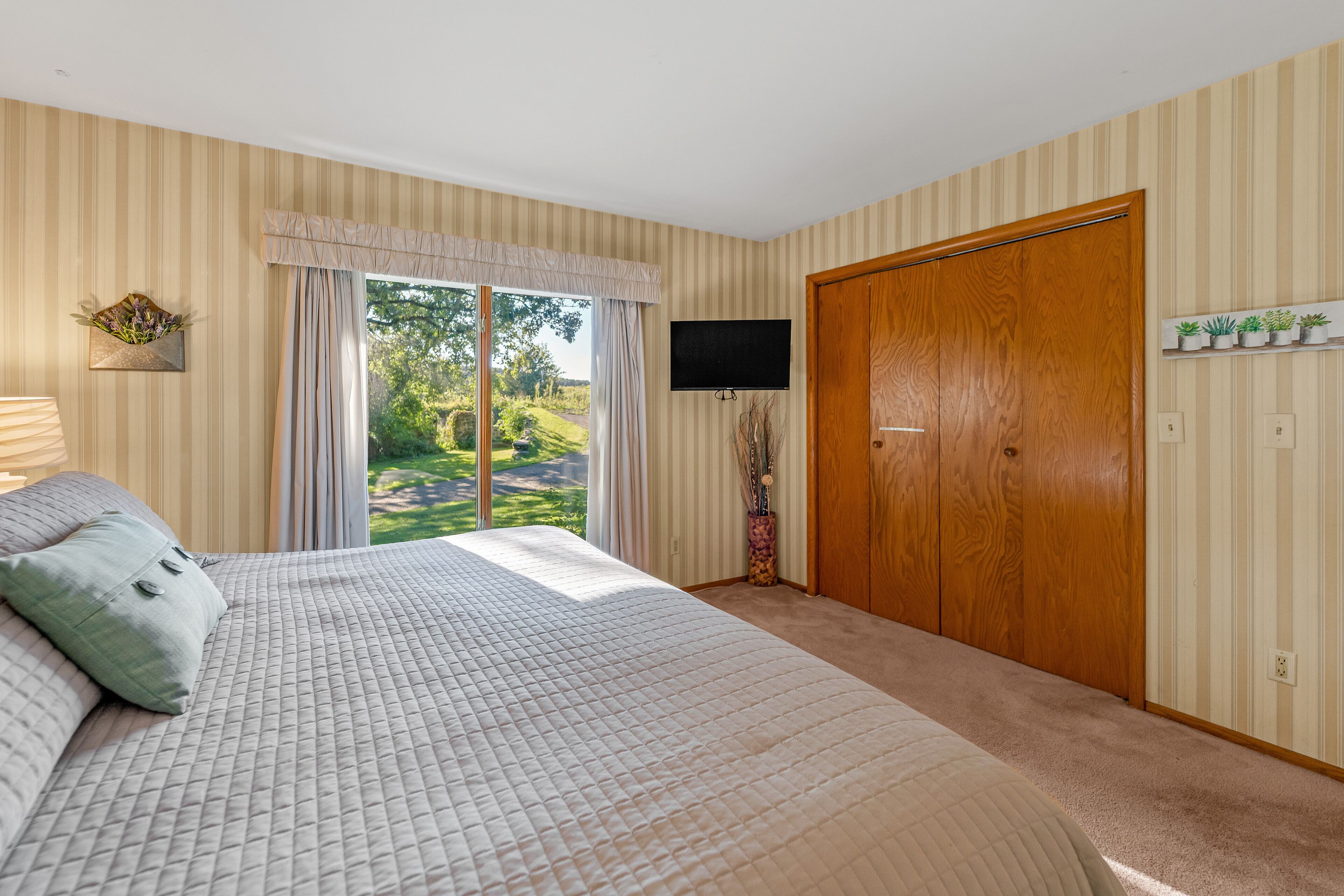 A bedroom with a large bed, a television, a wooden wardrobe, and a window with curtains.