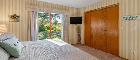 A bedroom with a large bed, a television, a wooden wardrobe, and a window with curtains.