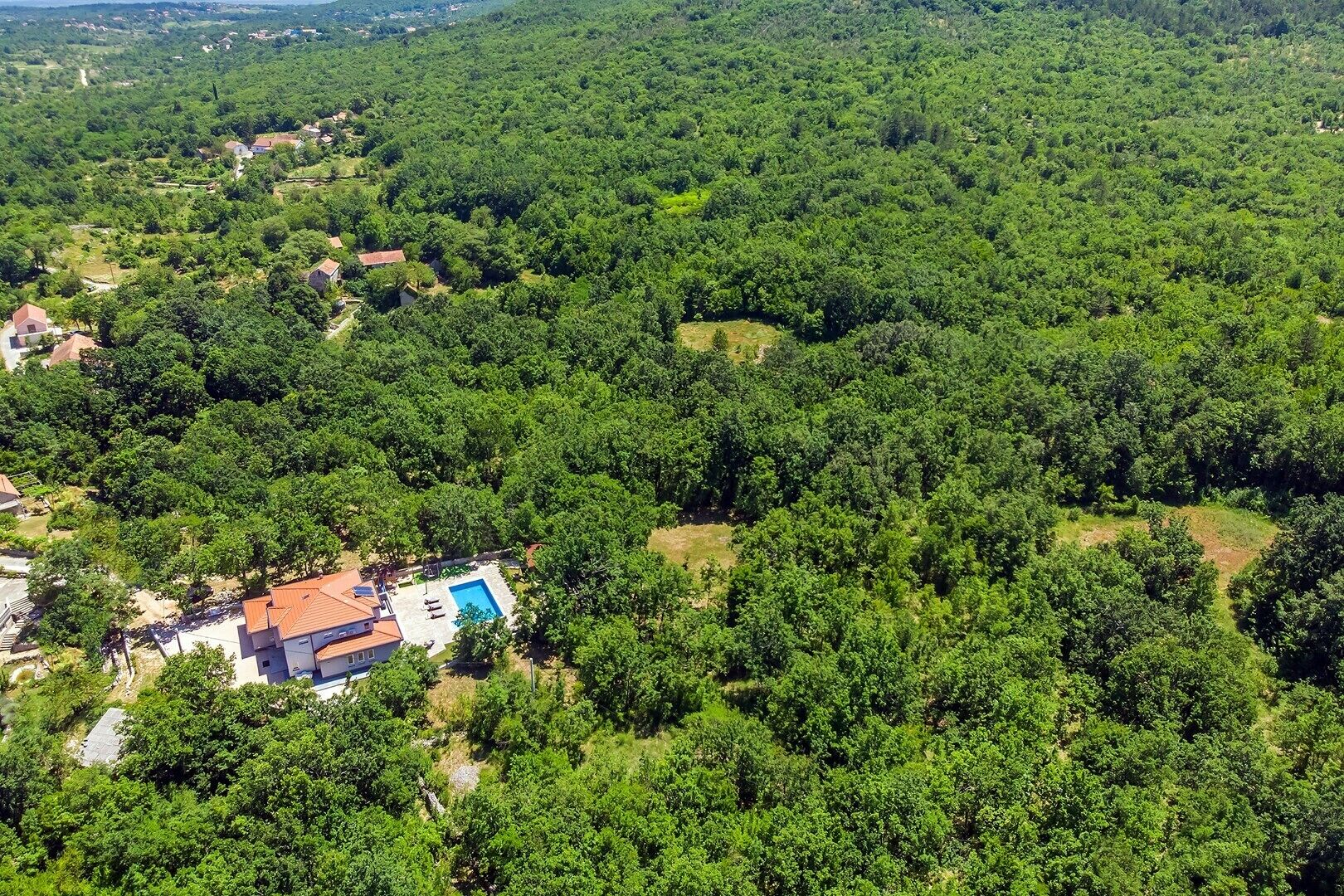 Vue aérienne d’une propriété entourée d’une forêt dense, avec un bâtiment doté d’une piscine.