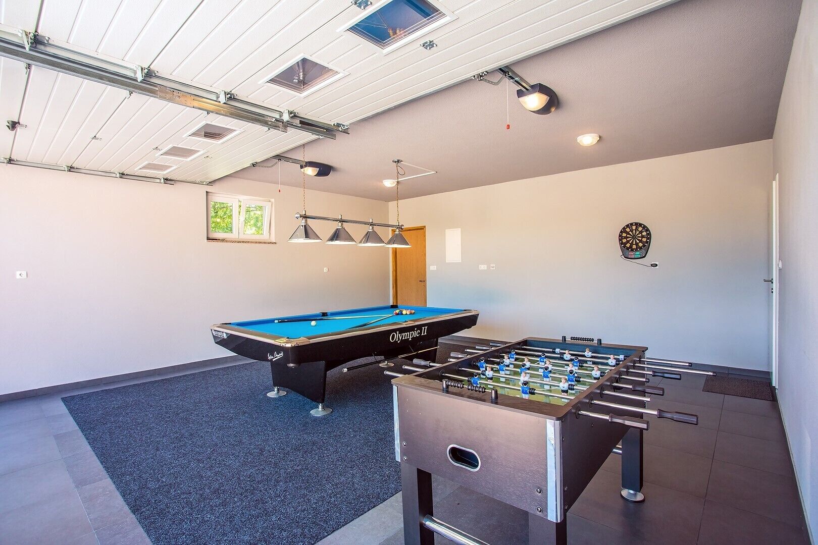 Una habitación con mesa de billar, mesa de fútbol de mesa, dardo y luces en el techo.