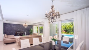 En moderne stue med et glasbord, beige sofaer og en lysekrone.