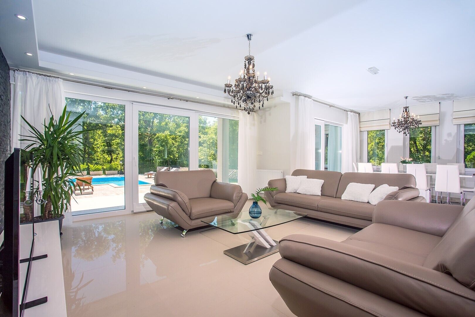 A spacious living room with a glass coffee table, two sofas, and a large window overlooking a pool.